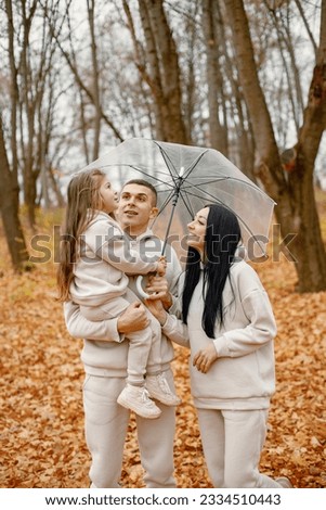 Young family standing in autumn forest under transparent umbrella