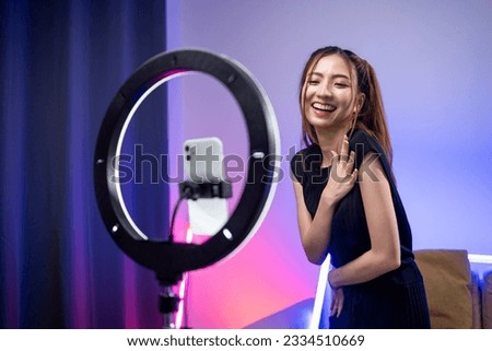Young trendy influencer asian woman dancing on mobile phone at home in living room with neon light. Creator vlogger talent dancing enjoy hobby content recording show video sharing on social media. Royalty-Free Stock Photo #2334510669