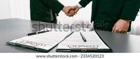 Focus closeup panorama business contract paper with pen, while two professionals shake hand in blurred background, signifying successful negotiation and partnership agreement with handshaking. Prodigy