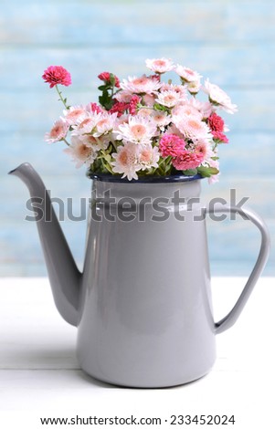 Beautiful flowers in pitcher on table on light blue background