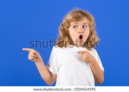 Excited kid boy on studio isolated background. Surprised face, amazed emotions of child. Kid boy pointing away on blue isolated studio background. Kid with index finger pointing, copy space.
