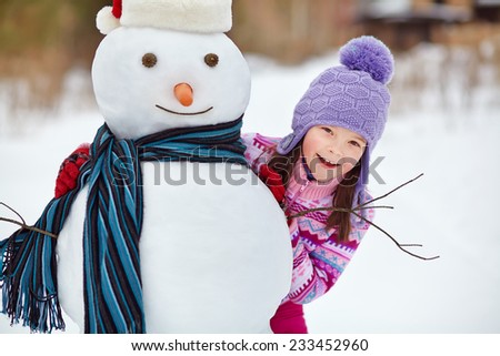 happy kid playing with snowman. funny little girl on a walk in the winter outdoors