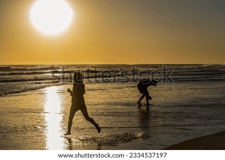 Silhouette of children playing in the sea water on the beach at sunset