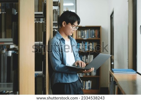 University Library: Beautiful smart asian university student uses Laptop, Writes Notes for Paper, Essay, Study for class assignment. Focused students learning, studying for college exams. Royalty-Free Stock Photo #2334538243
