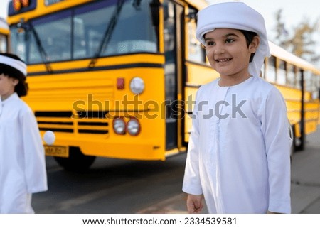 Emirati student near yellow school bus. Arabic boy in UAE kandura dishdash.  Royalty-Free Stock Photo #2334539581