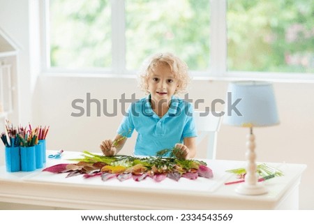 Child creating picture with colorful leaves. Art and crafts for kids. Little boy making collage image with rainbow plant leaf. Biology homework for young school student. Creative autumn home fun.