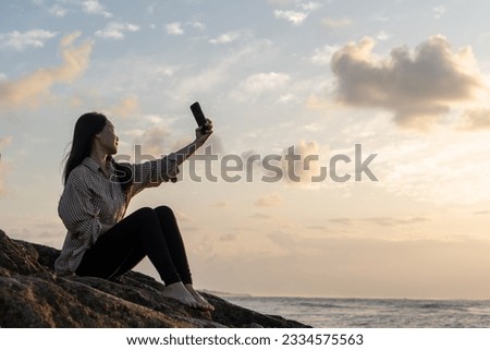 Side view woman looking at screen of mobile phone while sitting on the edge of beach rock