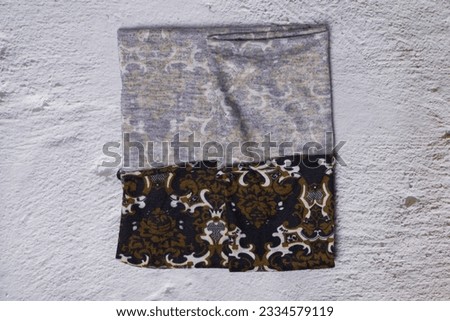 Buff anti-dust motocycle or motorbike with batik motifs in color white, black and army green with a gray cement as background.