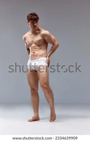 Full-length image of young man with healthy, strong, muscular body posing shirtless in underwear against grey studio background. Concept of man's beauty, sport, health, athletic body, medicine Royalty-Free Stock Photo #2334639909