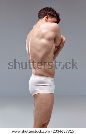 Back pains. Young man with relief, muscular, strong body, back posing shirtless in underwear against grey studio background. Concept of man's beauty, sport, health, athletic body, medicine Royalty-Free Stock Photo #2334639915
