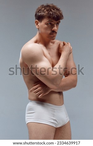 Handsome young man with muscular body posing shirtless in underwear against grey studio background. Relief hands. Concept of man's beauty, sport, health, athletic body, medicine Royalty-Free Stock Photo #2334639917