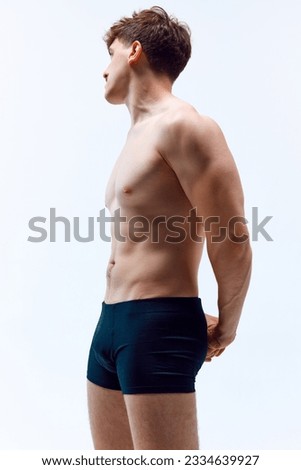 Side view portrait of young man with relief, muscular, healthy body posing shirtless in underwear against grey studio background. Concept of man's beauty, sportive and healthy lifestyle, athletic body Royalty-Free Stock Photo #2334639927