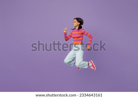 Full body side profile view happy active little kid teen girl 15-16 years old wears striped orange sweatshirt jump high run hurry up isolated on plain purple background. Childhood lifestyle concept