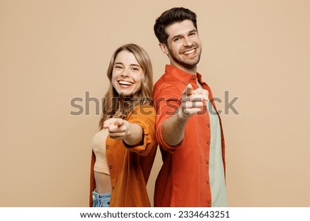 Side view young couple two friends family man woman wear casual clothes point index finger camera you stand back to back together isolated on pastel plain light beige color background studio portrait