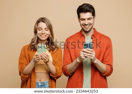 Young happy couple two friends family man woman wear casual clothes hold in hand use mobile cell phone together surfing internet isolated on pastel plain light beige color background studio portrait Royalty-Free Stock Photo #2334643253