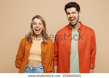 Young cool cheerful smiling happy couple two friends family man woman wear casual clothes looking camera wink blink eye together isolated on pastel plain light beige color background studio portrait
