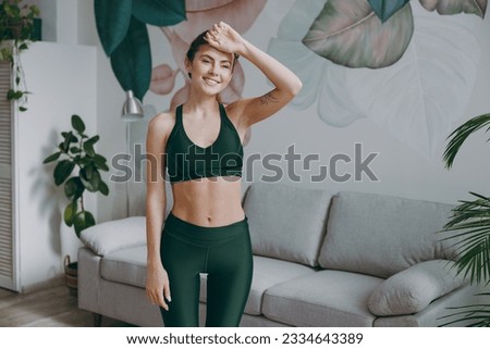 Young fun tired strong sporty athletic fitness trainer instructor woman wear green tracksuit put hand on forehead sweating training do exercises at home gym indoor. Workout sport motivation concept