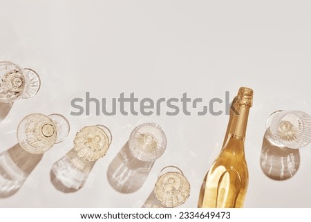 Summer party drinks flat lay, wine glasses with white sparkling wine and sunshine shadow on light table. Minimal pattern with beautiful wine glasses, above view still life, beige golden neutral color Royalty-Free Stock Photo #2334649473