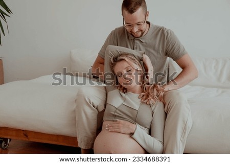 A man massages the neck of a pregnant woman in a bright apartment. High quality photo