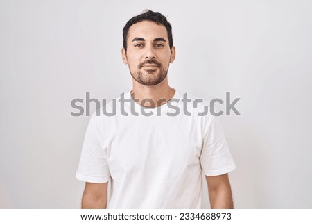 Handsome hispanic man standing over white background relaxed with serious expression on face. simple and natural looking at the camera. 