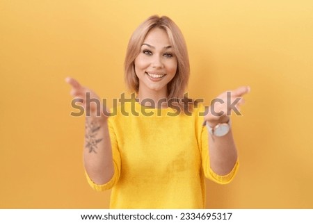 Young caucasian woman wearing yellow sweater smiling cheerful offering hands giving assistance and acceptance. 