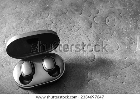 Black and white portrait of an open earphone, shot against a patterned black background