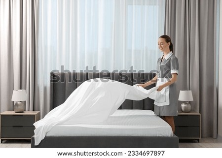 Young maid making bed in hotel room. Space for text Royalty-Free Stock Photo #2334697897
