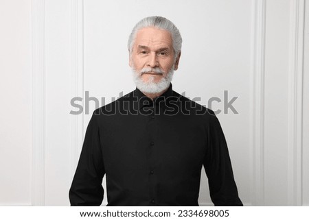 Portrait of handsome senior man near white wall