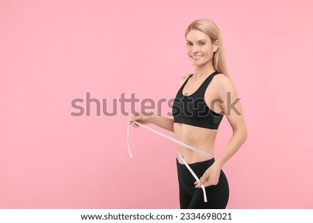 Slim woman measuring waist with tape on pink background, space for text. Weight loss Royalty-Free Stock Photo #2334698021