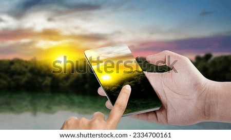 Man taking a picture with his mobile phone with a sunset scene background. World Photography Day 