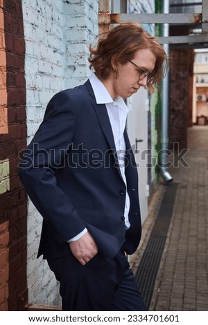 A handsome young man in a pantsuit. European. A college or university student. Street photo shoot near a brick wall