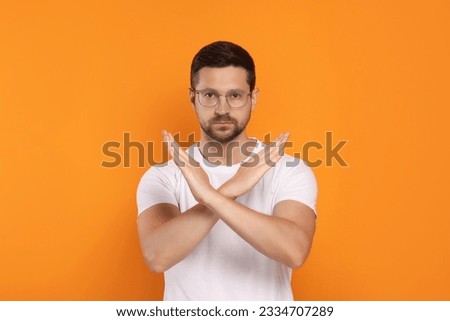 Handsome man with crossed hands on orange background. Stop gesture