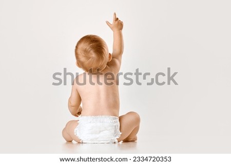 Back view image of little baby, child, toddler sitting in diaper against white studio background. Curious baby. Concept of childhood, newborn lifestyle, happiness, care. Copy space for ad Royalty-Free Stock Photo #2334720353