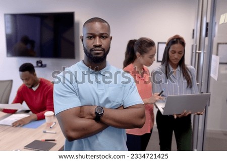 Portrait of young african american businessman with arms crossed against colleagues in boardroom. unaltered, business, teamwork and modern office concept. Royalty-Free Stock Photo #2334721425