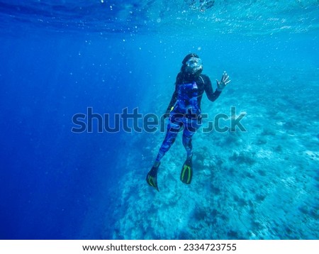 A girl in a swimming suit and with fins is engaged in free diving at a deep water near the big reef