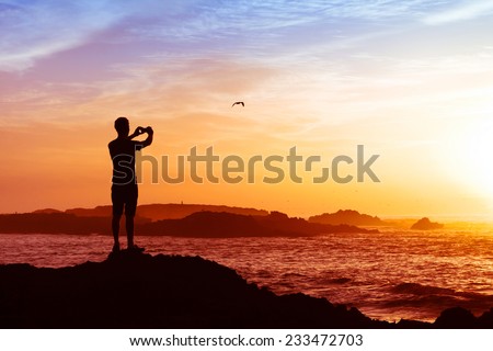 man taking photos of sunset with mobile phone