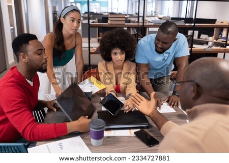 Young biracial colleagues listening to african american businessman's strategy during meeting. unaltered, business, teamwork and modern office concept. Royalty-Free Stock Photo #2334727881