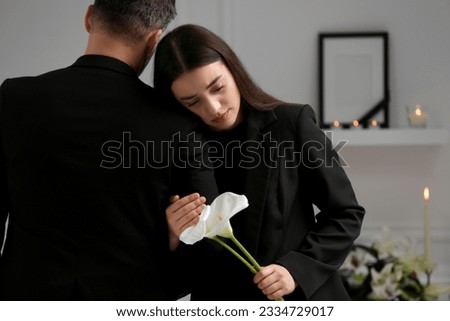 Sad couple with calla lily flowers mourning indoors, space for text. Funeral ceremony Royalty-Free Stock Photo #2334729017