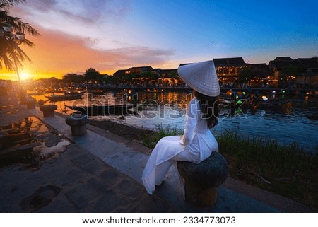 Vietnamese women in national costumes sitting Beautiful night view at the ancient town. Vietnam. Hoi An. Street view with traditional boats and lifestyle on the background of the ancient town. Royalty-Free Stock Photo #2334773073