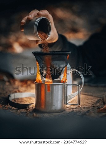 A hand pouring smashed coffee powder into metal cup with a filter, making campig coffee