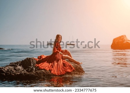 Woman travel sea. Happy tourist in red dress enjoy taking picture outdoors for memories. Woman traveler posing on the rock at sea bay surrounded by volcanic mountains, sharing travel adventure journey