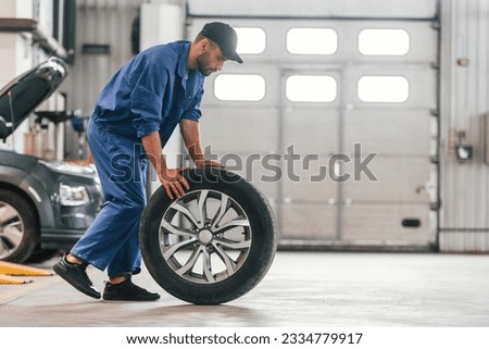 Side view. Moving the new tire. Auto mechanic working in garage. Repair service. Royalty-Free Stock Photo #2334779917