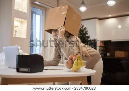 Young entrepreneur is holding cardboard boxes and place it on her head after successfully in sale products while sitting on comfortable the couch and working in living room at home office