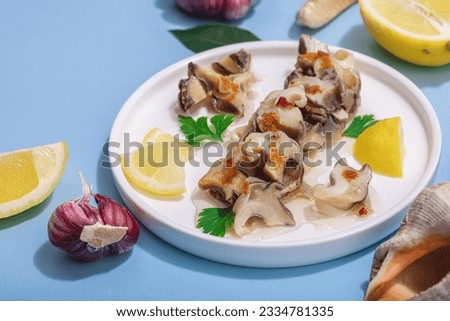 Pickled rapan meat with oil, spices and greens. Healthy seafood rich of omega. Marine decorative prop, hard light, dark shadow, blue background, close up Royalty-Free Stock Photo #2334781335