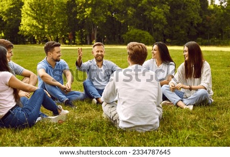 Friendship and communication. Group of young people communicate sitting on grass in park on summer sunny day. Group of male and female friends laughing and talking while sitting in circle outdoors.