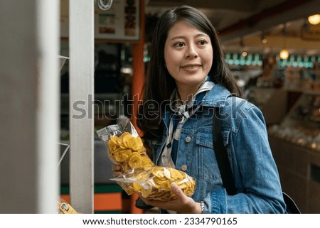 Asian customer female is choosing sweet dry bananas in organic shops. woman holding food and looking around with a smile. Royalty-Free Stock Photo #2334790165