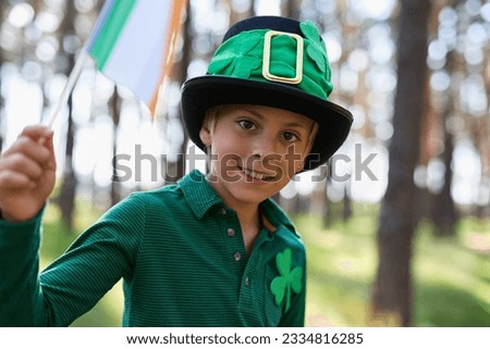 Happy little leprechaun celebrating St Patricks Day. Portrait of a cute white kid waving with flag of Ireland dressed in green