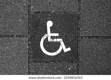 A sign for the disabled painted on the street. Black and white.