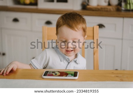 Child watching cartoons online on phone at home alone. Toddler playing mobile device video game. Cute little boy using smartphone, looking at screen. Kid gen Z using parental control app on cell phone