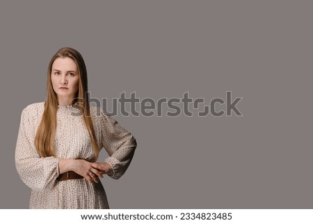 Beautiful girl with folded hands looking at camera. Young serious woman isolated on beige wall with copy space. Closeup portrait of lady in dress looks confident on grey background.